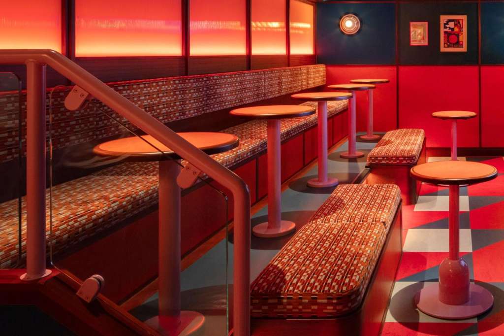 Sports bar booth seating with red upholstered benches, illuminated signage, and checkered floor in warm lighting.