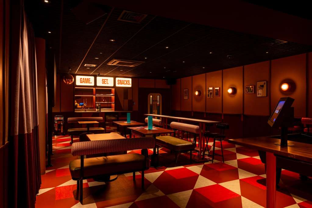 Games room with red and cream diamond flooring, neon signage, ping pong tables, and warm ambient lighting.