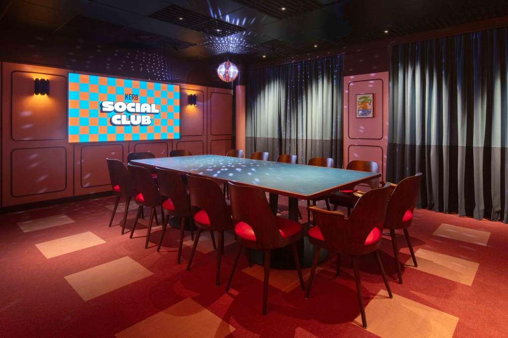 Modern meeting room with long illuminated table, red chairs, and branded display screen in warm lighting.
