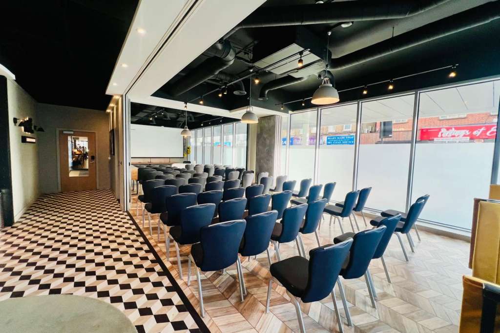 Modern meeting room with rows of blue chairs facing a whiteboard, pendant lighting, and floor-to-ceiling windows.