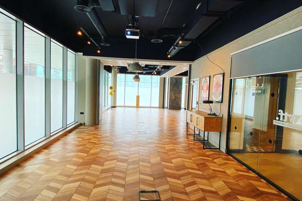 Modern event space with herringbone wood flooring, floor-to-ceiling windows, black ceiling with exposed services, and glass partition walls.