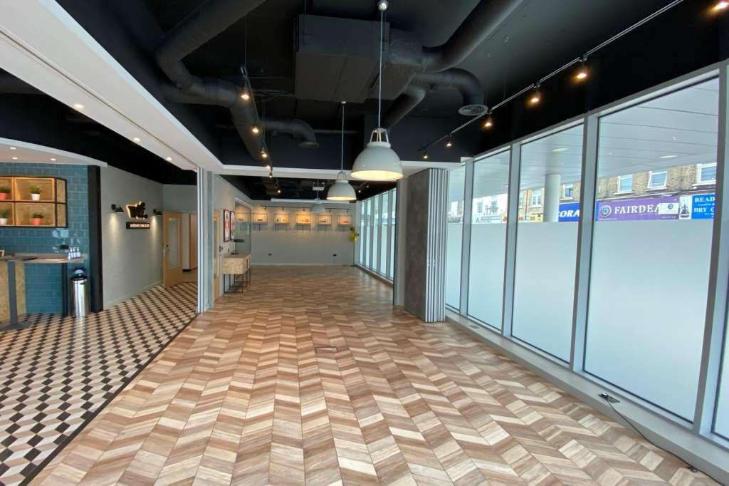 Modern event space with herringbone flooring, exposed ceiling, pendant lighting, and glass partition walls.