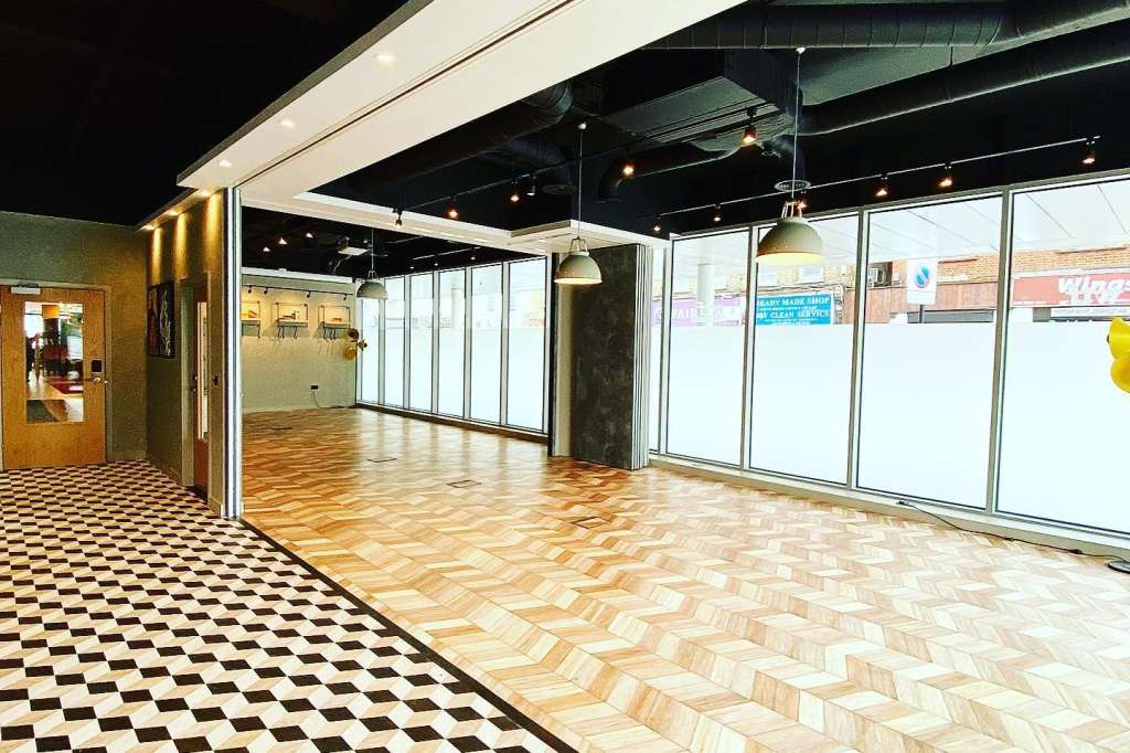 Modern event space with herringbone wood flooring, large windows, pendant lighting, and open layout.