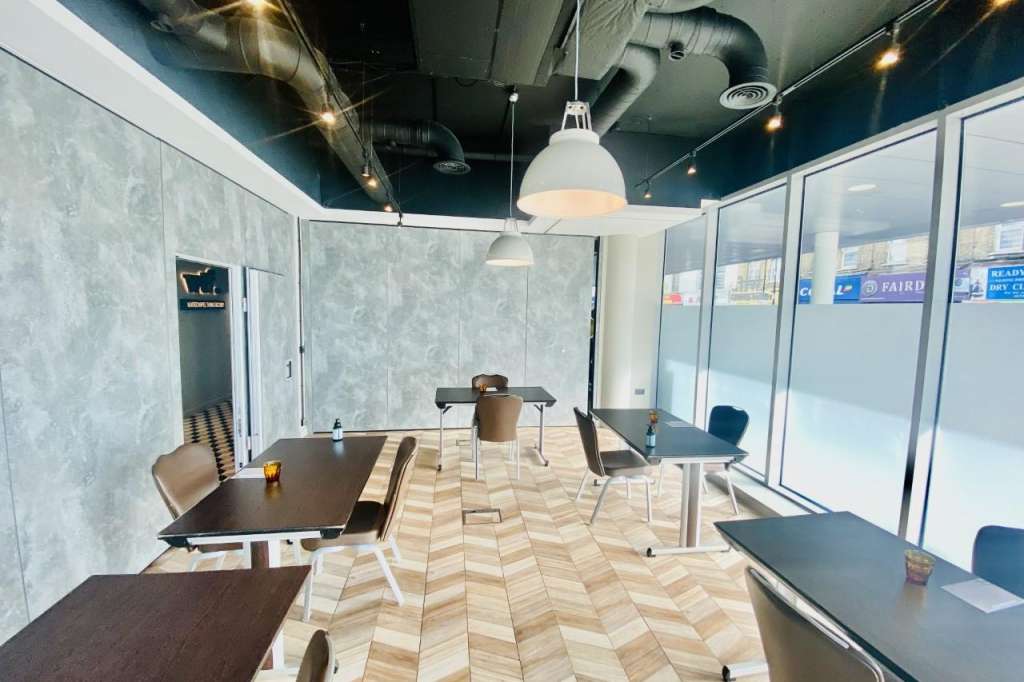 Modern meeting space with multiple dark tables, chairs, herringbone flooring, pendant lighting, and glass partition walls.