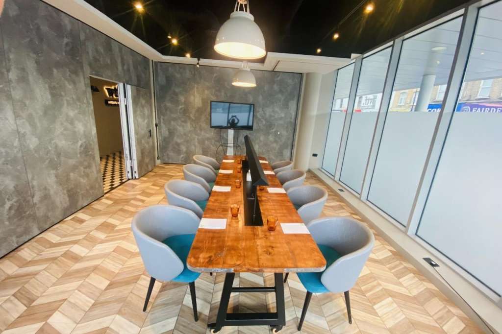 Modern meeting room with long wooden table, blue chairs, pendant lighting, and glass partition walls.