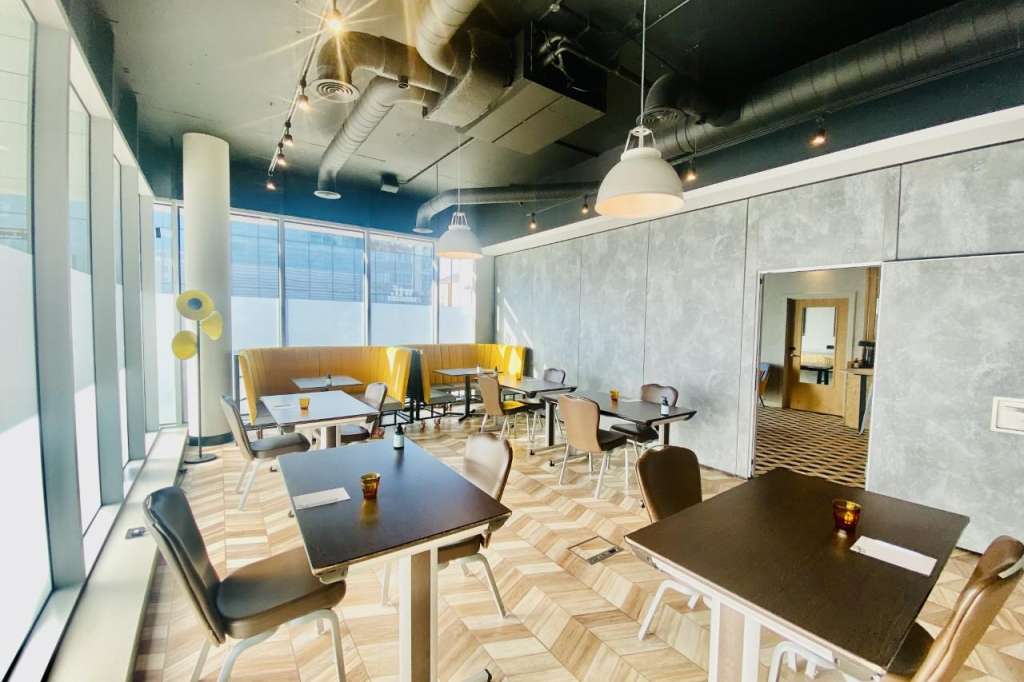 Modern meeting space with black tables, yellow seating booths, pendant lighting, and floor-to-ceiling windows.