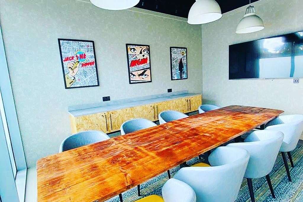 Modern meeting room with long wooden table, white chairs, pendant lighting, and pop-art wall decor.