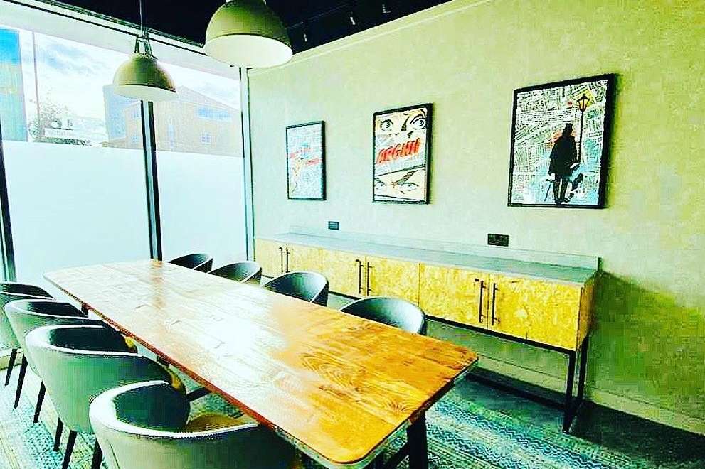 Modern meeting room with long wooden table, green chairs, pendant lighting, and framed artwork on lime walls.
