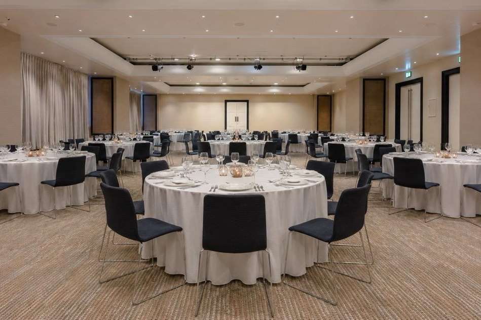 Ballroom set up for a formal seated dinner with round tables, white linens, black chairs, and recessed ceiling lighting.
