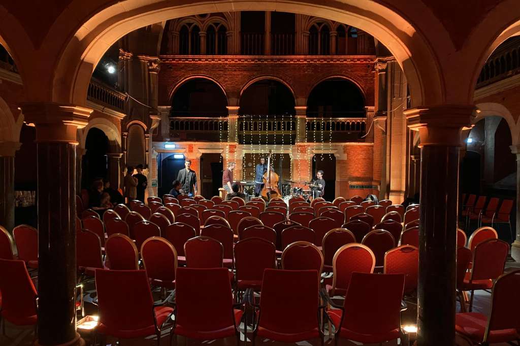 Historic auditorium with red seating rows facing a stage with performers and decorative lighting.