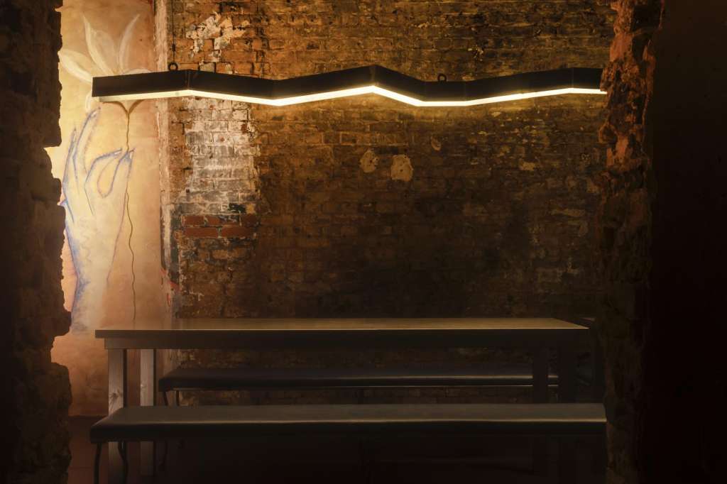 Industrial brick room with exposed beams, modern linear lighting fixture, and wooden bench seating.