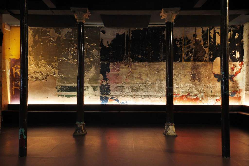 Industrial interior with large illuminated windows displaying textured artwork and atmospheric lighting.