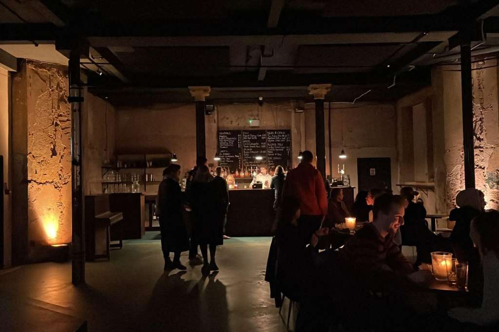 Industrial venue with exposed brick, warm lighting, bar counter, and guests mingling during evening event.