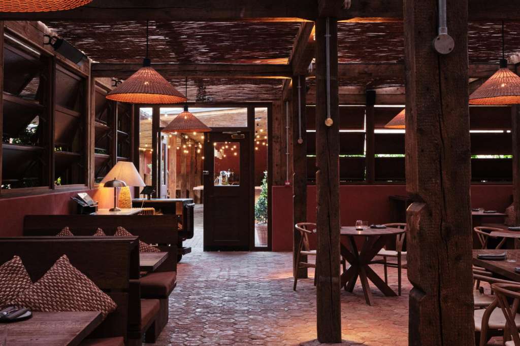 Terrace with wooden pergola, ambient lighting, dining tables and chairs, warm evening ambiance.