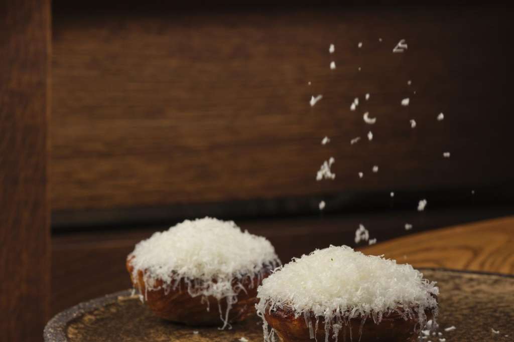 Two coconut-topped pastries on a dark plate with powdered sugar dusting, wooden surface visible.