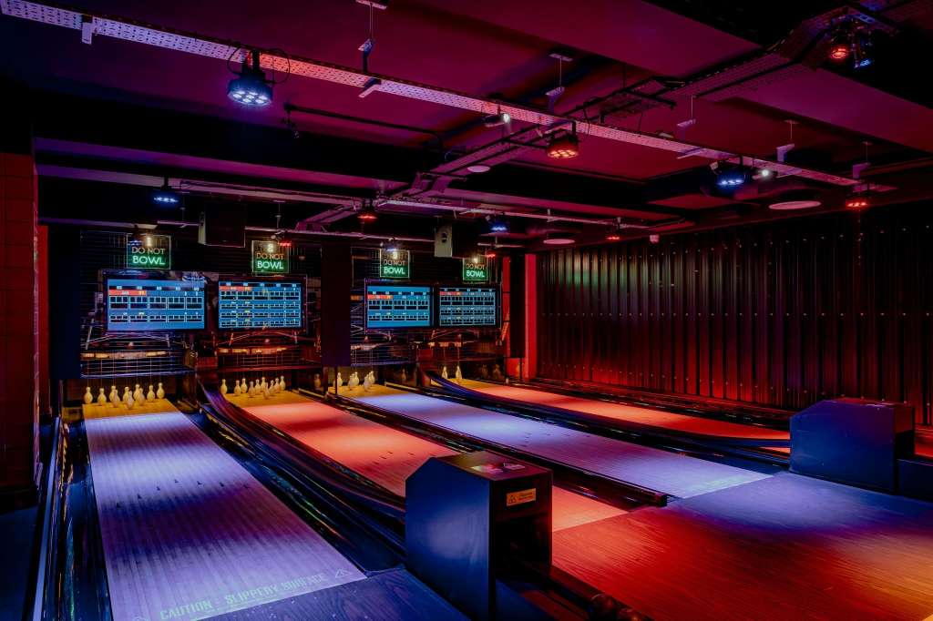 Bowling alley with multiple lanes, neon signage, and colorful LED lighting on ceiling and lanes.