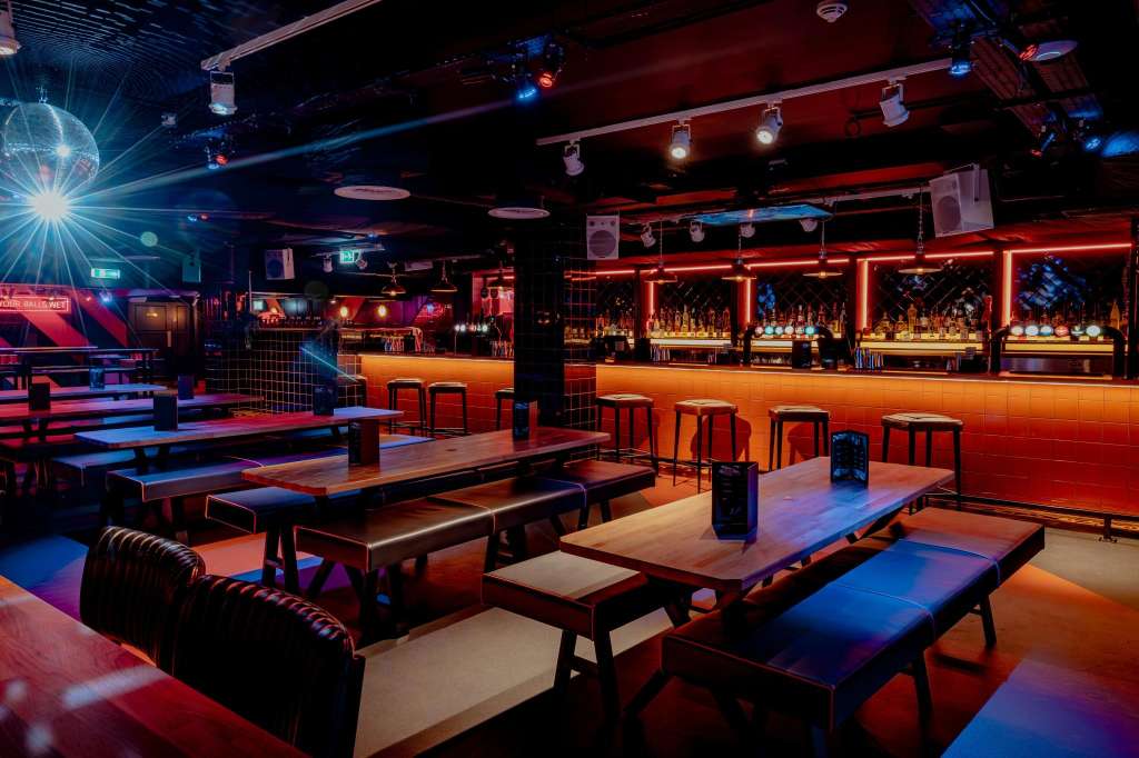 Modern nightclub interior with neon red and blue lighting, bar counter, lounge seating, and dance floor.