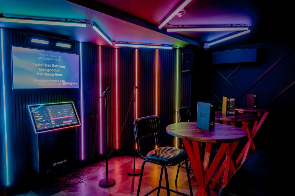 Modern event space with neon lighting, DJ booth, round tables, and colorful ambient lighting throughout.