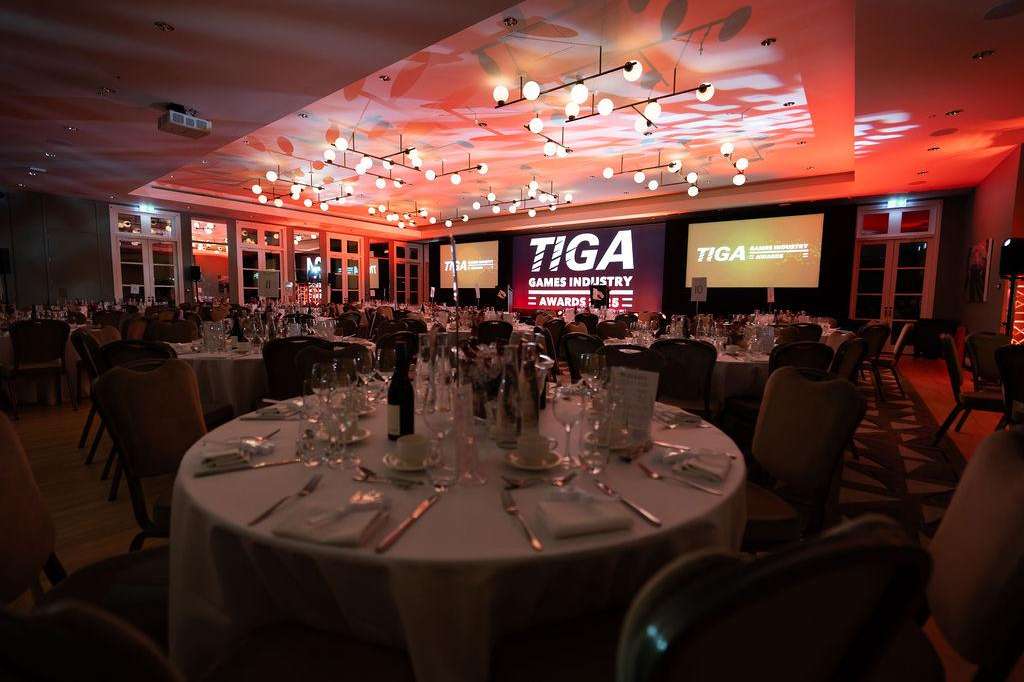 Ballroom set for seated dinner with round tables, place settings, and red ambient lighting with projection screens.