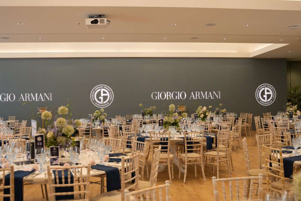 Ballroom set for a formal dinner with round tables, chiavari chairs, floral centerpieces, and branded backdrop.