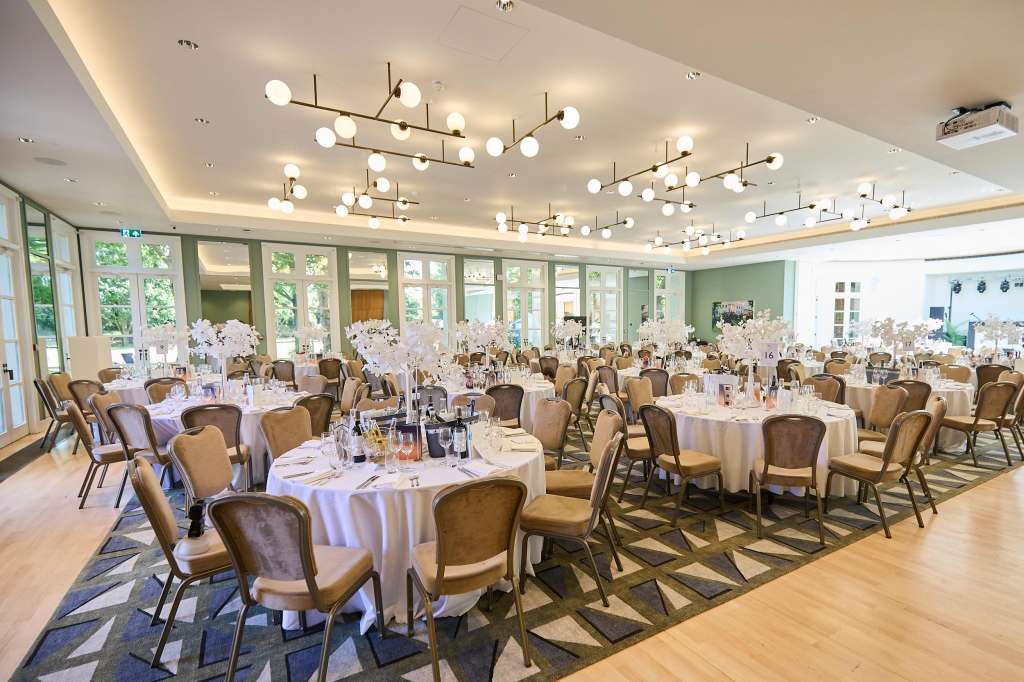 Elegant dining room set with round tables, white linens, gold chairs, and modern pendant lighting.