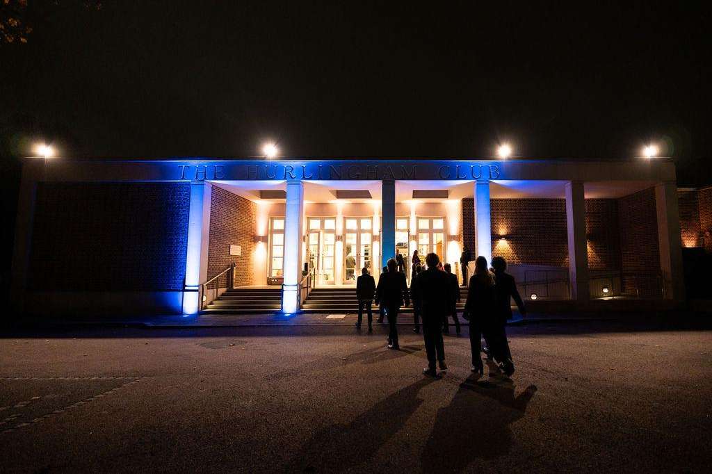 Exterior venue entrance at night with blue uplighting, illuminated columns, and guests gathered outside.
