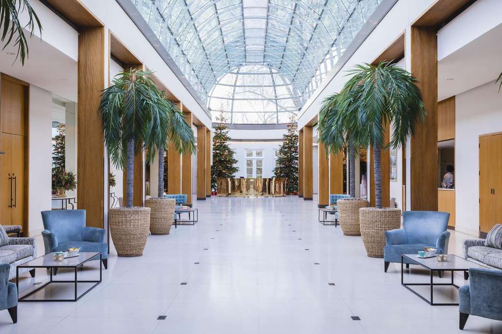Palm Court with glass roof, wooden columns, potted palms, and blue seating areas arranged symmetrically.