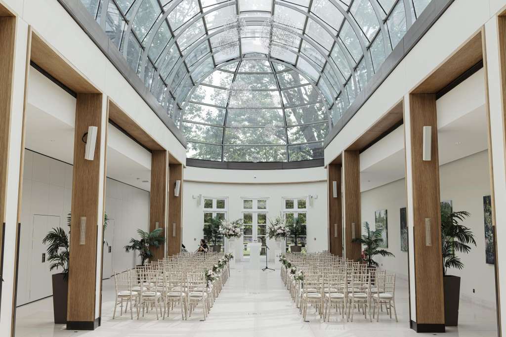 Palm Court with glass roof, wooden columns, rows of chairs, floral arrangements, and natural light from skylights.