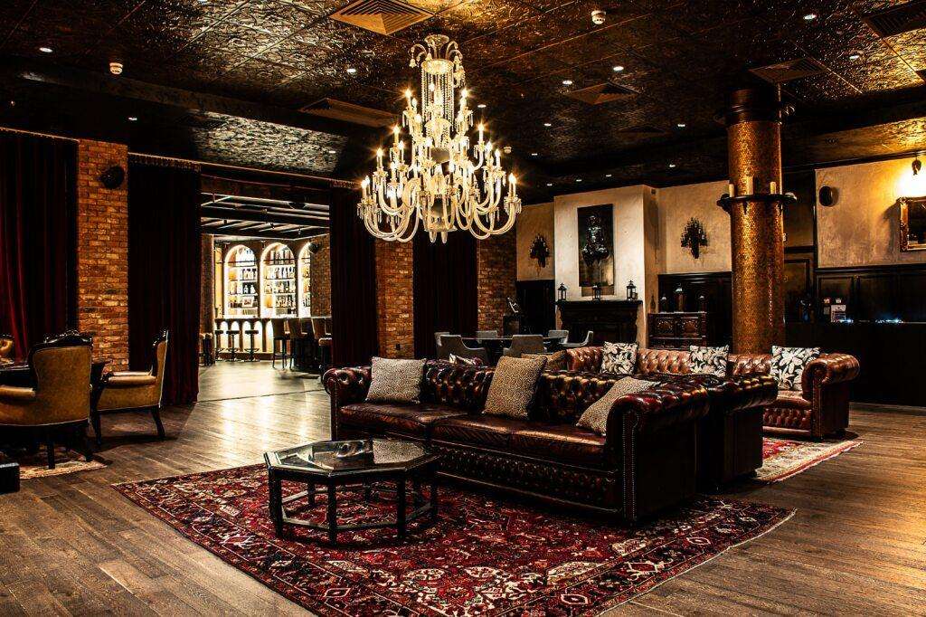 Rooftop restaurant lounge with leather Chesterfield sofa, crystal chandelier, exposed brick, and ornate rugs.
