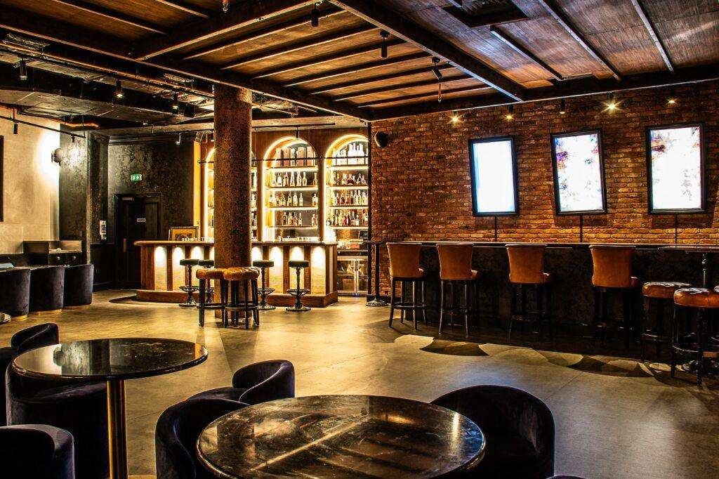 Rooftop restaurant with exposed brick, bar seating, round tables, and warm ambient lighting.