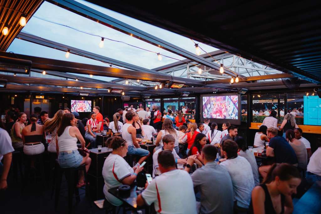 North Terrace with large crowd, high ceilings, glass roof panels, ambient lighting, and screens displaying content.