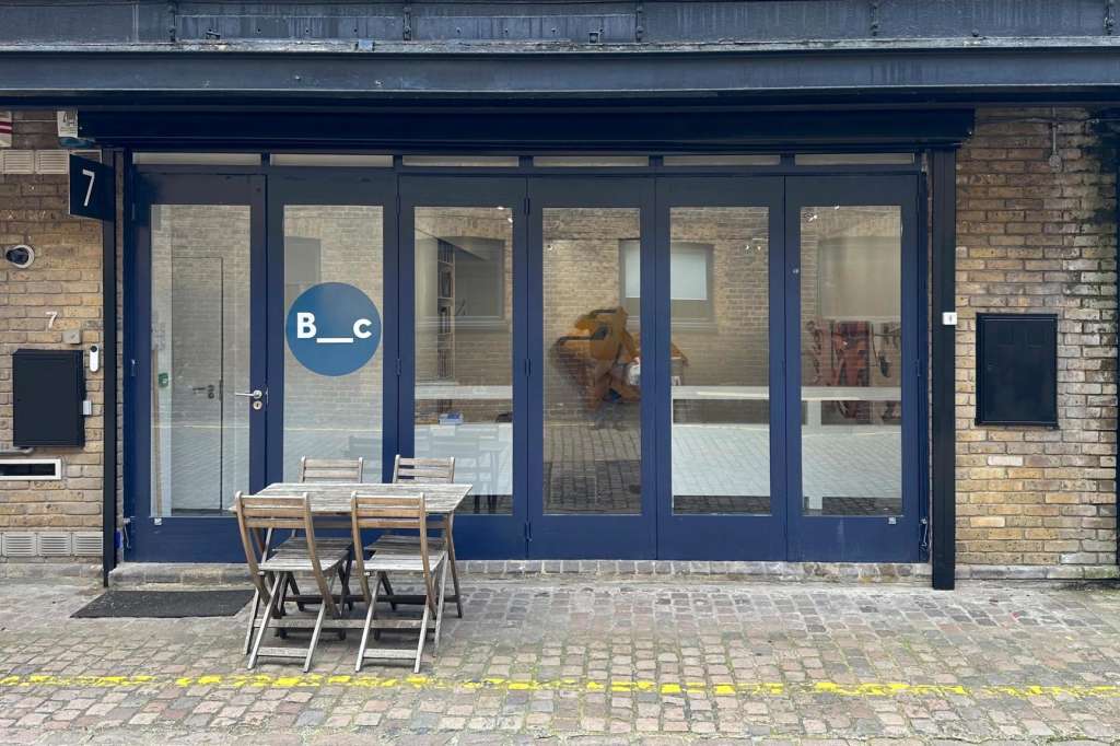 Contemporary gallery storefront with blue framing, large windows, and minimal exterior seating.