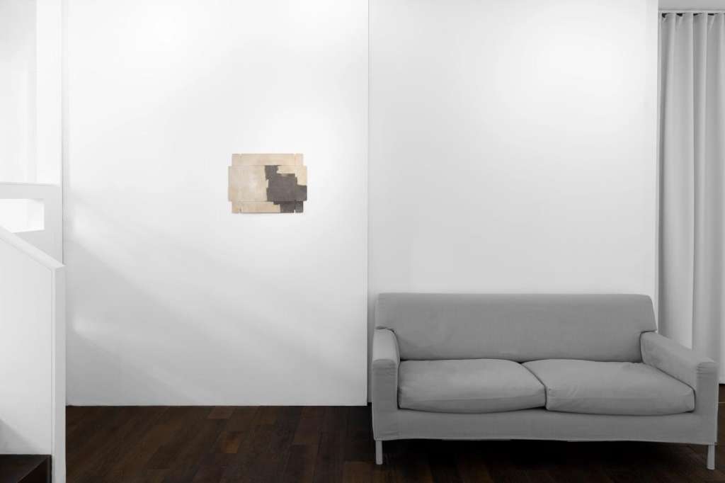 Gallery space with white walls, abstract artwork, gray sofa, and floor-to-ceiling curtains.
