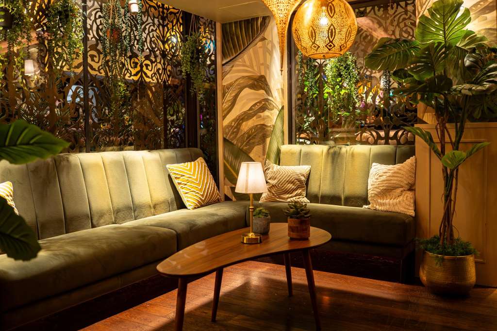 Lounge Bar with cream upholstered seating, wooden coffee table, decorative screens, potted plants, and warm ambient lighting.