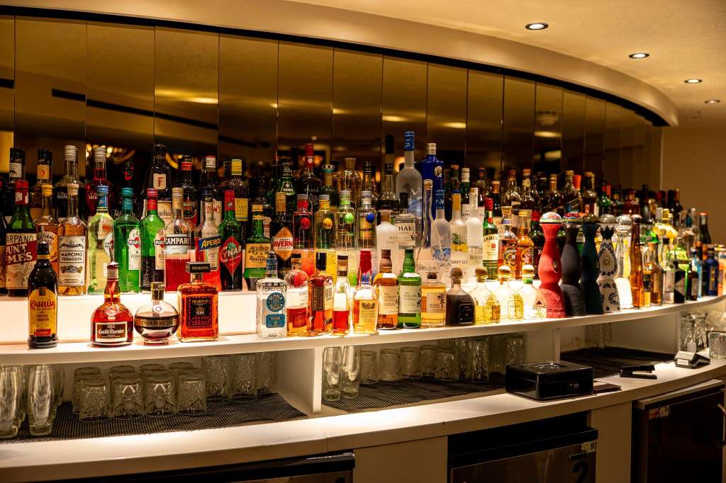 Lounge Bar with extensive bottle display behind curved counter, warm lighting, and mirrored backdrop.