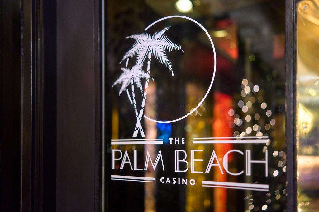 The Palm Beach Casino logo on glass entrance door with palm tree graphic and blurred interior lights.