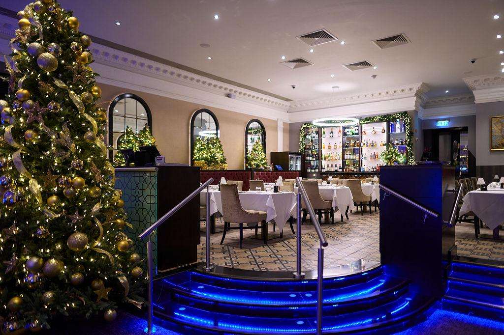Dining room with round tables, white linens, and a decorated Christmas tree with gold ornaments and purple lighting.