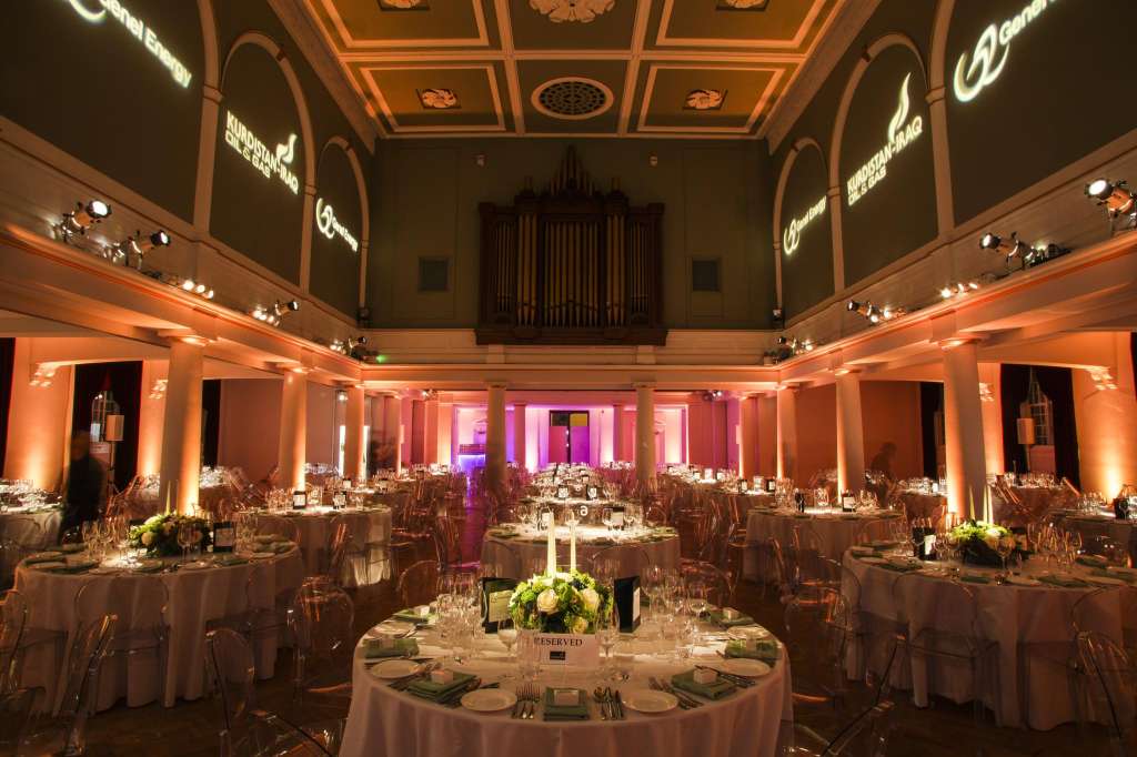 Soane Hall set up for a formal dinner with round tables, white linens, ambient uplighting, and an organ backdrop.