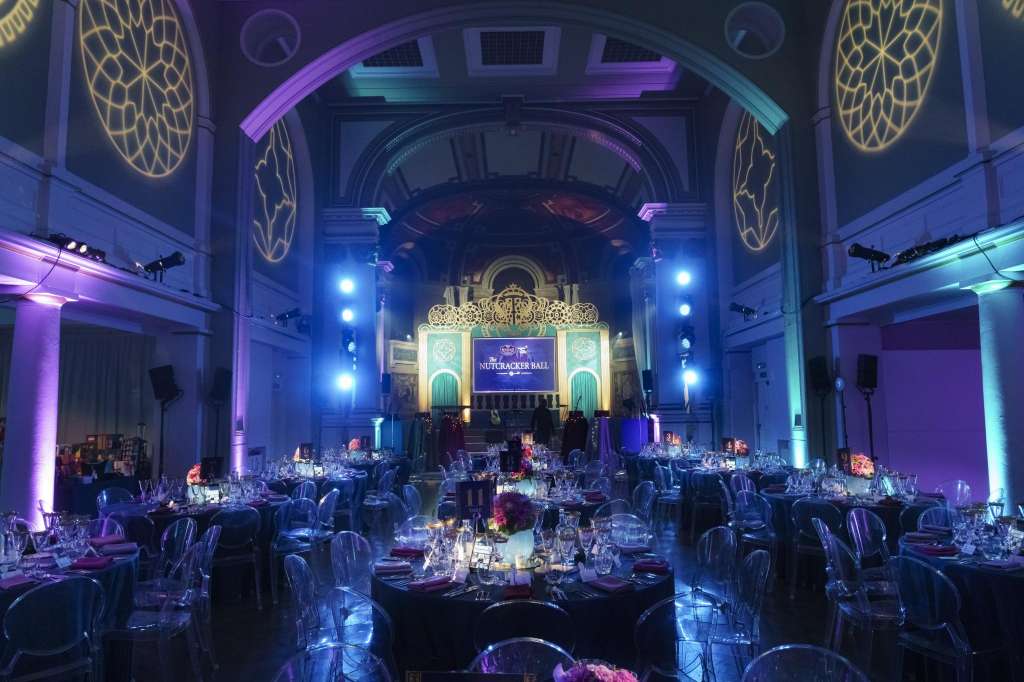 Soane Hall set up for a formal dinner with round tables, dramatic purple and blue lighting, ornate ceiling details, and a stage backdrop.