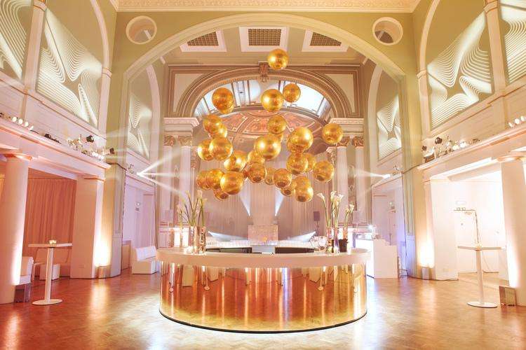 Grand hall with ornate ceiling, golden sphere chandelier, and circular bar counter with ambient lighting.