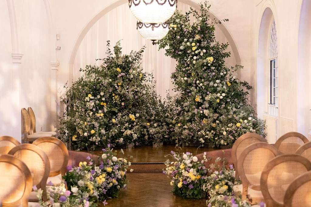 Soane Hall decorated with white and yellow floral installations, wooden chairs lining the aisle, ornate chandeliers overhead.