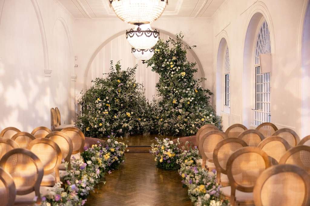 Soane Hall set up for an event with rows of wooden chairs, large floral installations with yellow and white flowers, and decorative garland.