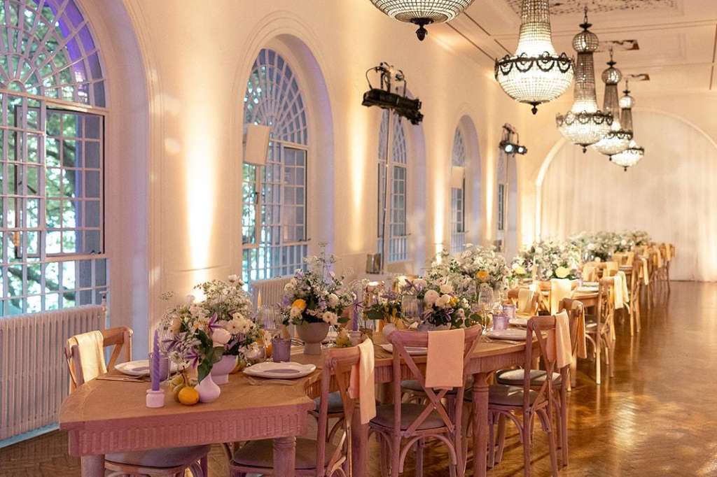Soane Hall set for a seated dinner with long tables, pink chairs, floral centerpieces, and ornate chandeliers.