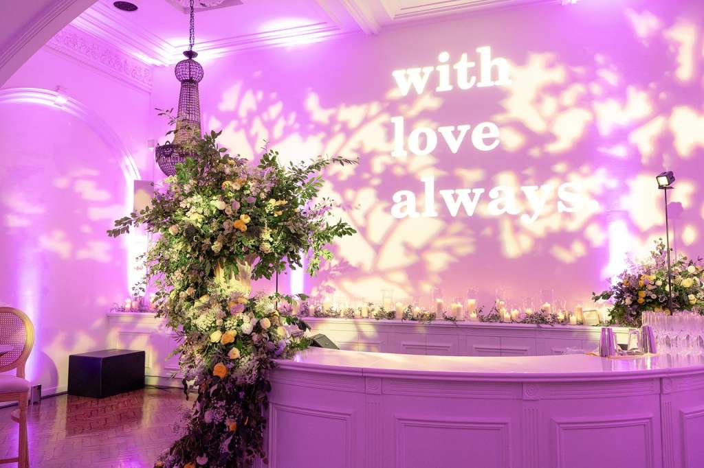 Soane Hall with purple ambient lighting, ornate chandelier, floral installations, and decorated bar counter.