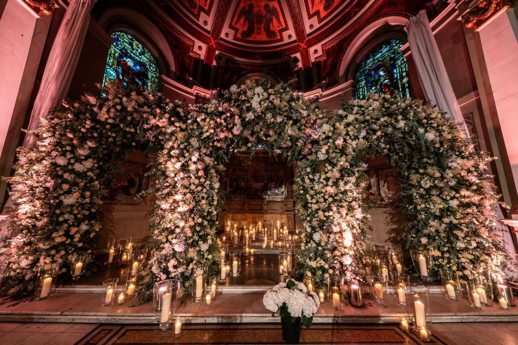 Soane Hall decorated with elaborate floral arch and candlelit arrangement under ornate ceiling with stained glass windows.