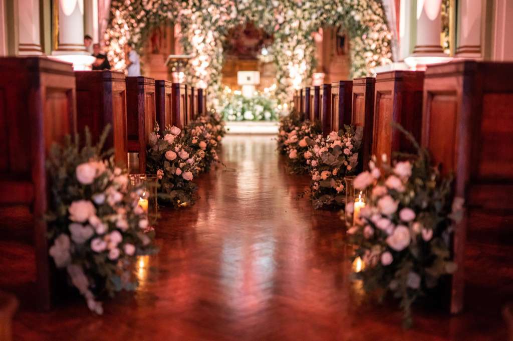 Soane Hall aisle decorated with pink floral arrangements, greenery garland overhead, and candlelit pews.
