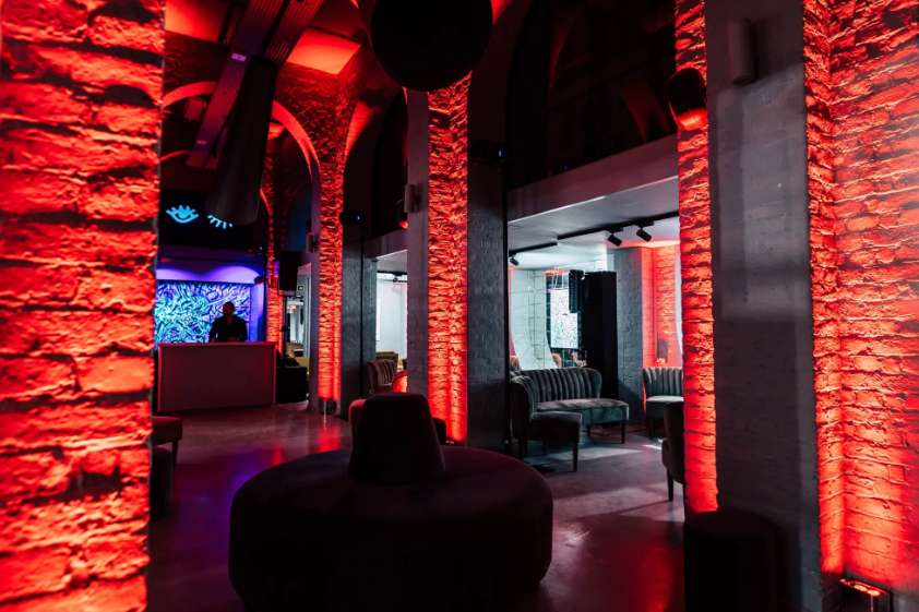 Gallery space with red uplighting on exposed brick walls, modern seating, and atmospheric ambient lighting.