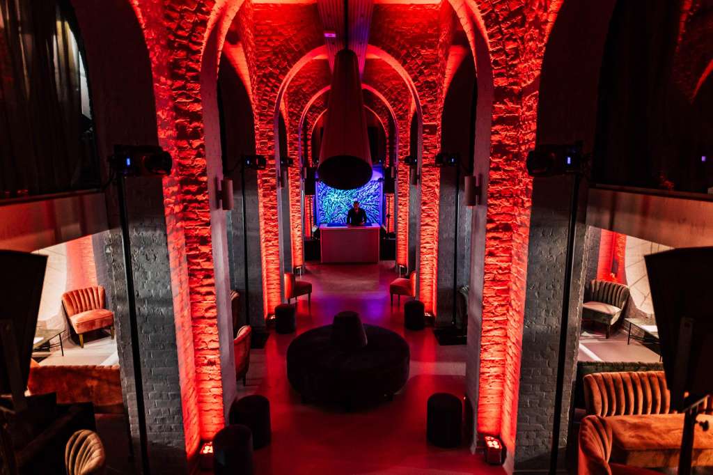 The Soane Hall with dramatic red uplighting on stone arches, modern seating, and blue accent lighting at far end.