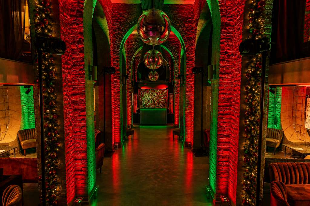 Gallery space with red and green uplighting on exposed brick columns, disco balls, and modern seating along the sides.