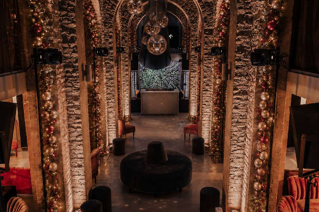 The Soane Hall with brick arches, warm string lighting on columns, black seating, and festive red accents.